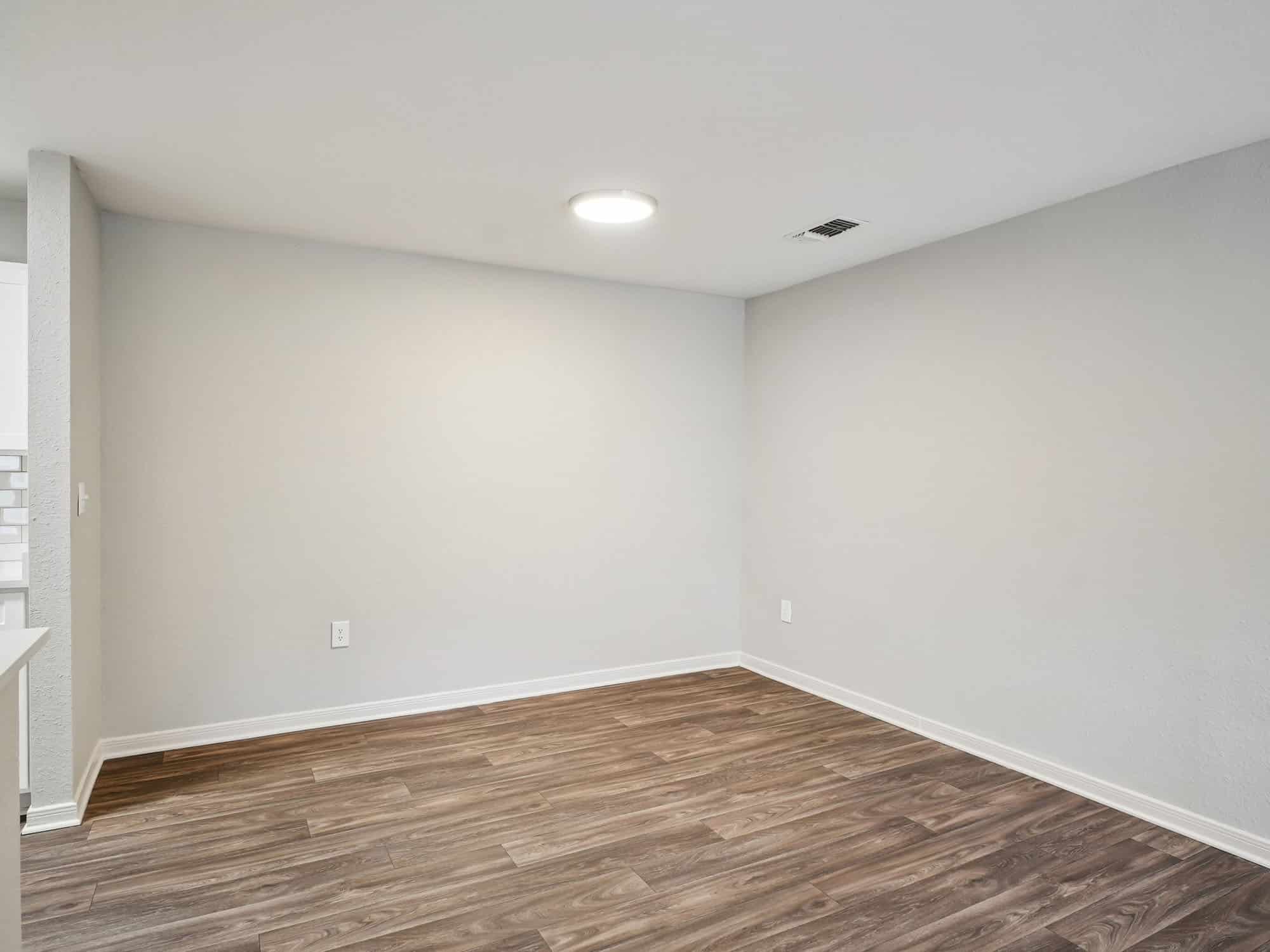 Empty room with light gray walls, wood-style flooring, a round ceiling light, and an air vent on the ceiling.