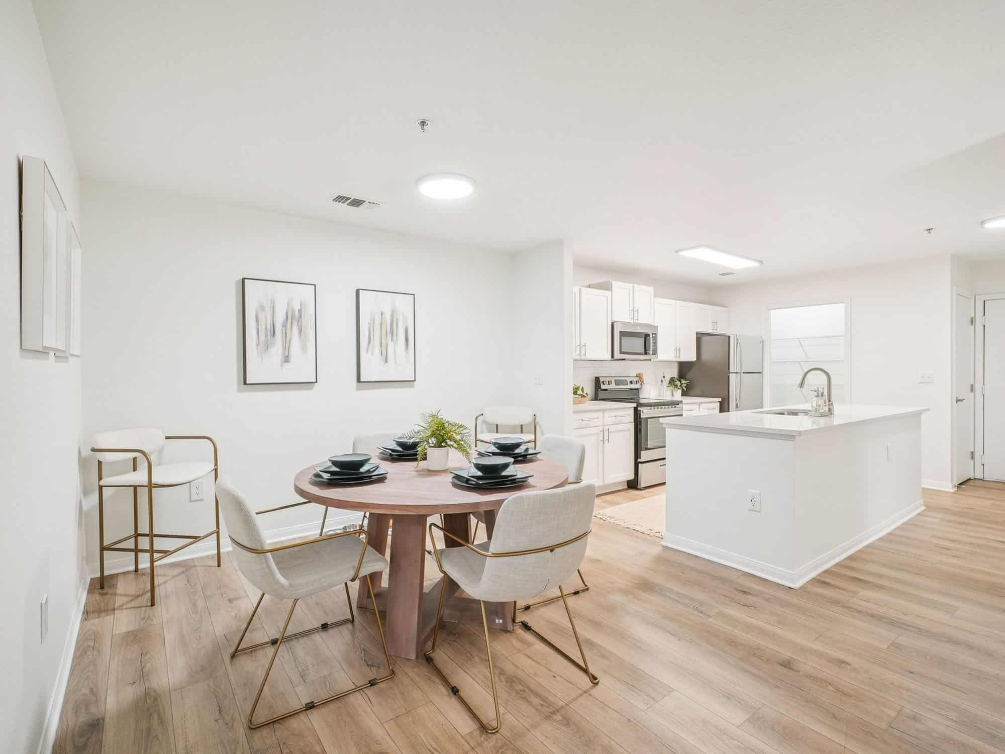 Open-concept kitchen and dining area with light wood floors, a round dining table set for four, modern appliances, and minimalist decor.